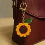 Handmade crochet sunflower keychain attached to a brown leather bag with green leaf and yellow petals
