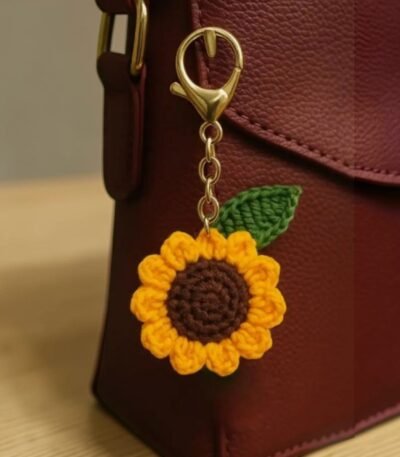 Handmade crochet sunflower keychain attached to a brown leather bag with green leaf and yellow petals