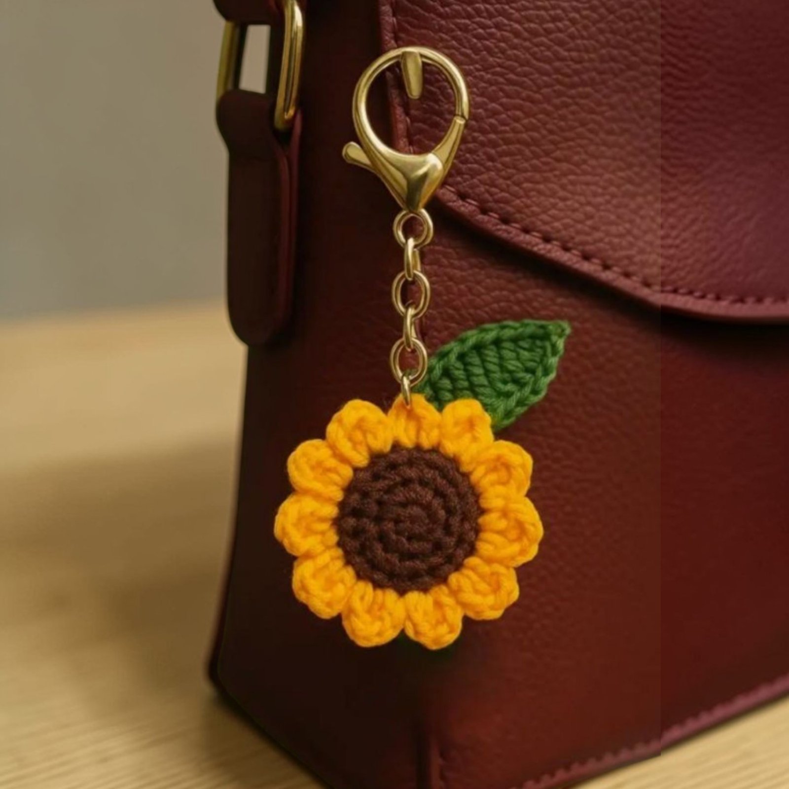 Handmade crochet sunflower keychain attached to a brown leather bag with green leaf and yellow petals