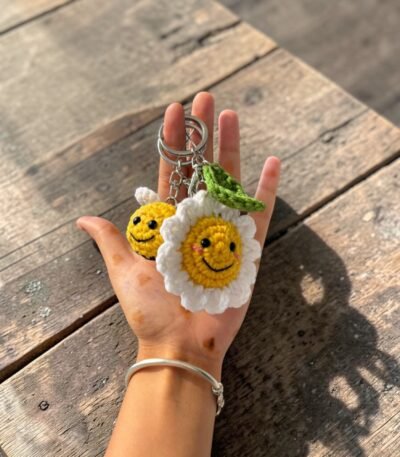 handmade crochet smiling daisy flower keychain with green leaf held in hand