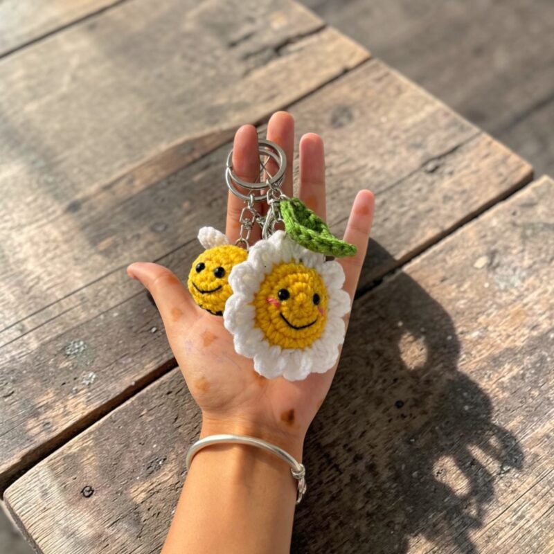 handmade crochet smiling daisy flower keychain with green leaf held in hand