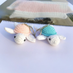 Two handmade crochet turtle keychains in pastel colors placed on a white surface