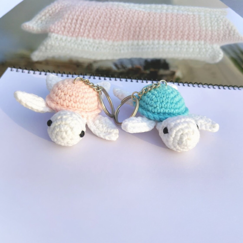 Two handmade crochet turtle keychains in pastel colors placed on a white surface